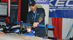 Danny Hacker, trainer for Keco Body Repair Products, sprays alcohol to release the glue from a centipede-type pull tab at a demonstration using the K-Beam Bridge Lifter at the 2022 Northeast trade show.