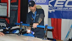 Danny Hacker, trainer for Keco Body Repair Products, sprays alcohol to release the glue from a centipede-type pull tab at a demonstration using the K-Beam Bridge Lifter at the 2022 Northeast trade show.