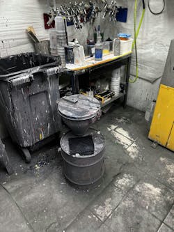 This paint mix room shows a couple violations: the plastic trash can needs to be a metal one with a closed metal lid, and the liquid solvent paint-waste container needs to be grounded and include a waste-paint label.