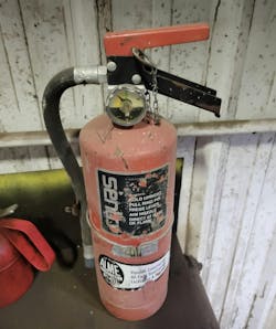 This fire extinguisher is out of service, as evidenced by the arrow not in the green. It also needs to be mounted, not loose on a table. It is also missing a fire extinguisher sign above it and needs to be tagged by the servicing company to indicate when it was last serviced.